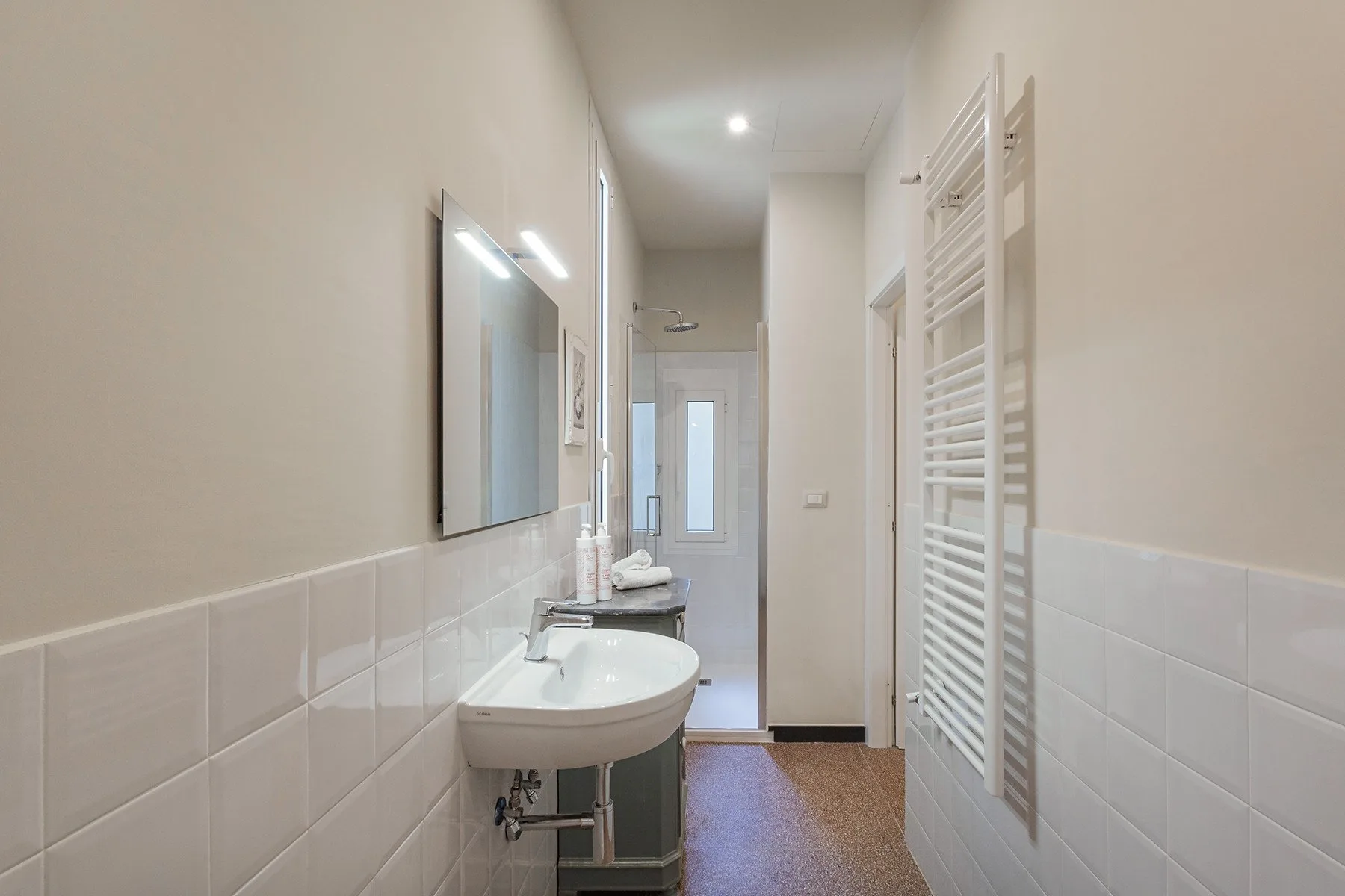 A narrow bathroom has a sink, mirror, and wall-mounted towel rack.