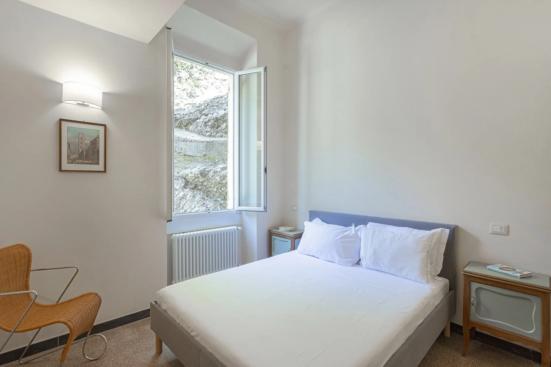 A bright bedroom with a neatly made bed beside an open window.