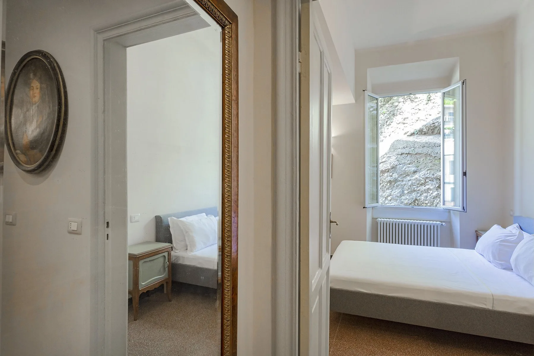 A bedroom with a bed beside an open window overlooking a stone wall.