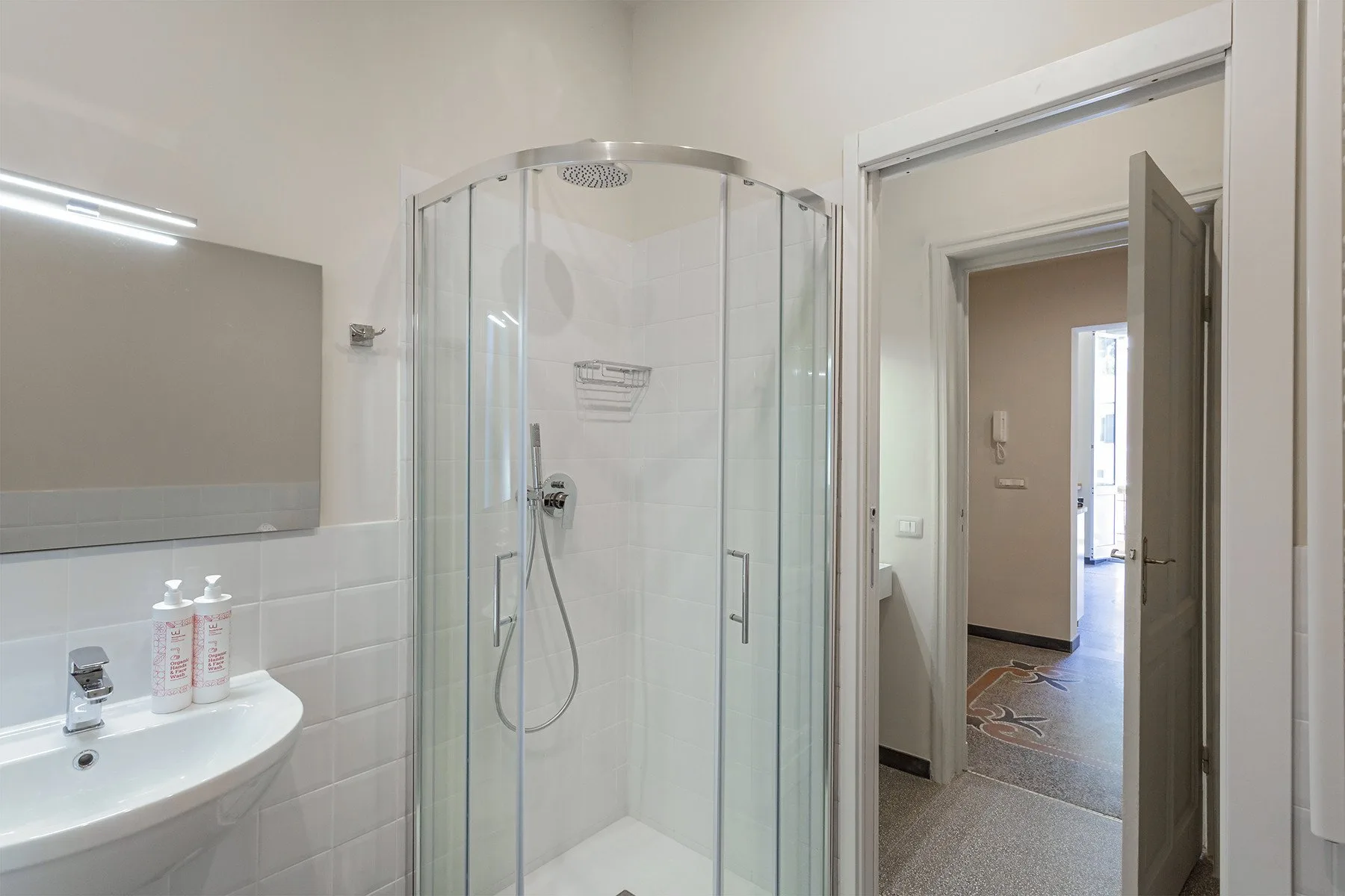 A bright bathroom with a glass shower and a sink beside the doorway.