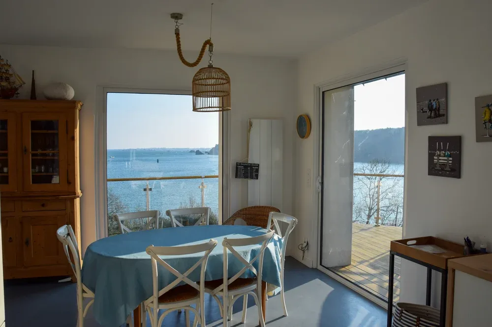 A dining area with a table beside large windows overlooking the water.