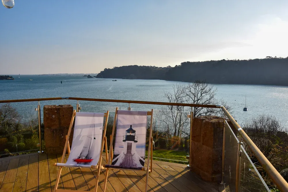 A wooden deck overlooks a calm bay, with two lounge chairs facing the water.
