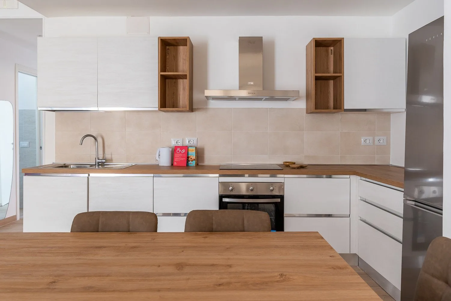 Una cocina moderna con gabinetes blancos, una placa de cocina y una mesa de madera.