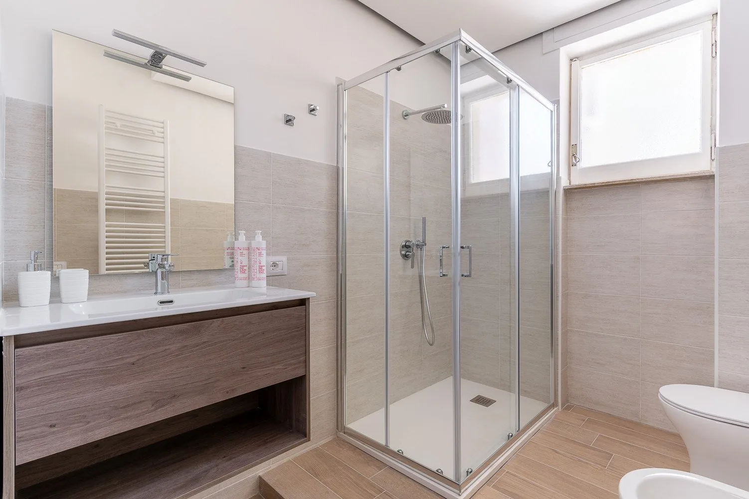Un baño luminoso con ducha de vidrio, lavabo y ventana.