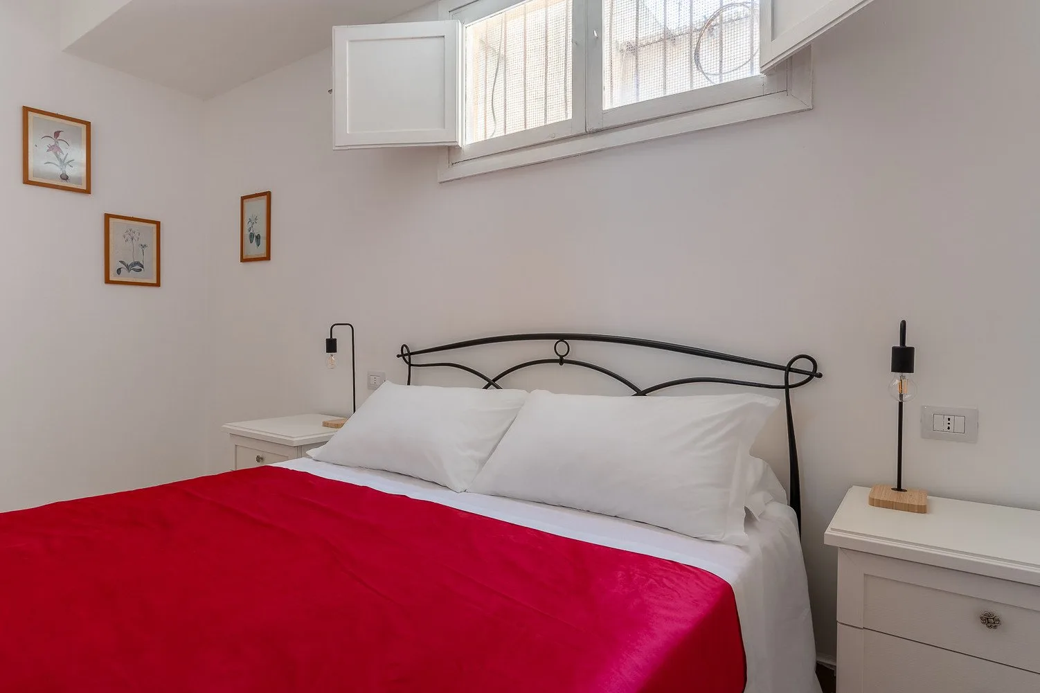 Un dormitorio con una cama vestida con ropa de cama blanca y una manta roja brillante.