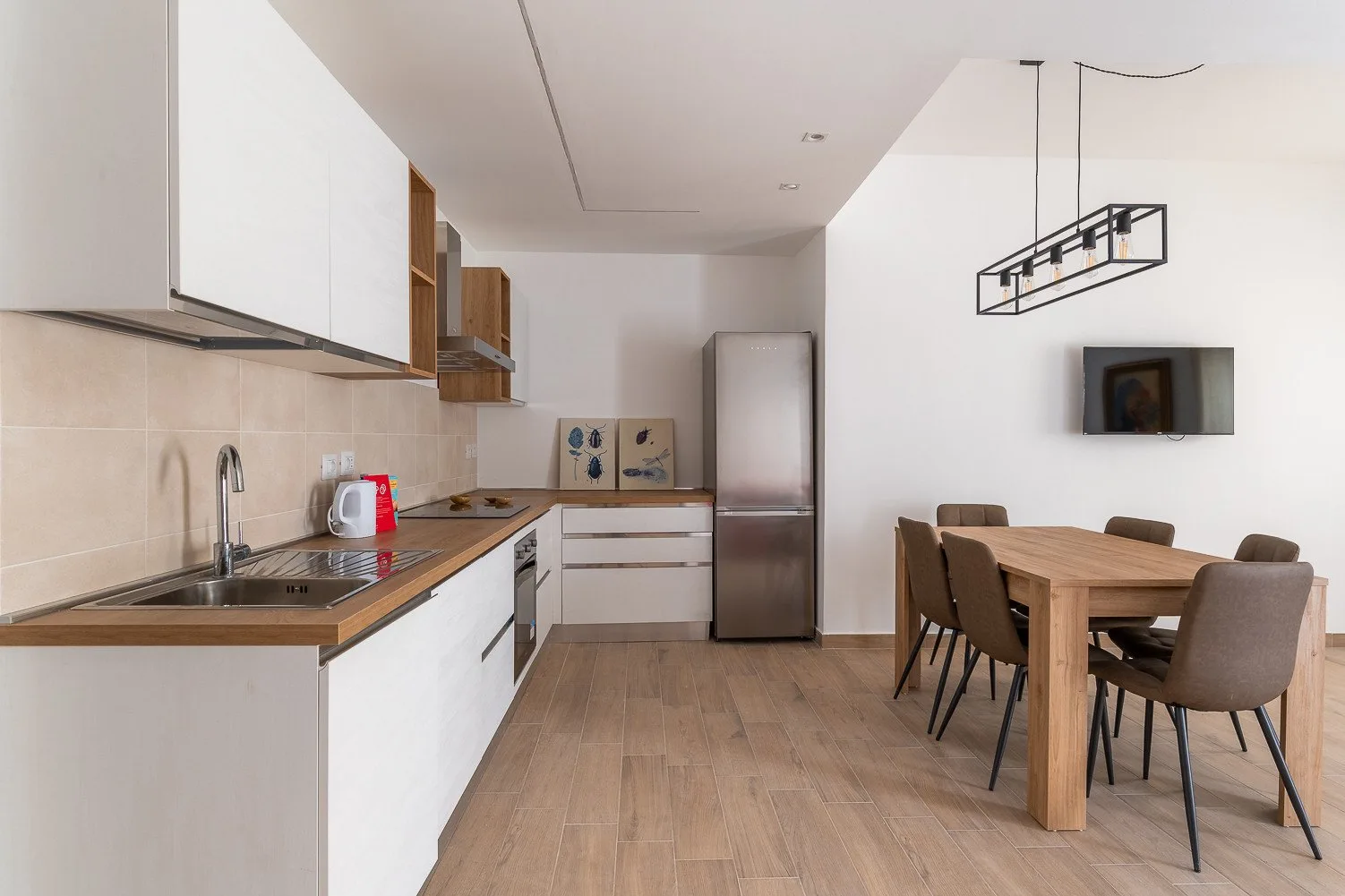 Una cocina luminosa con comedor, mesa de madera y armarios blancos.