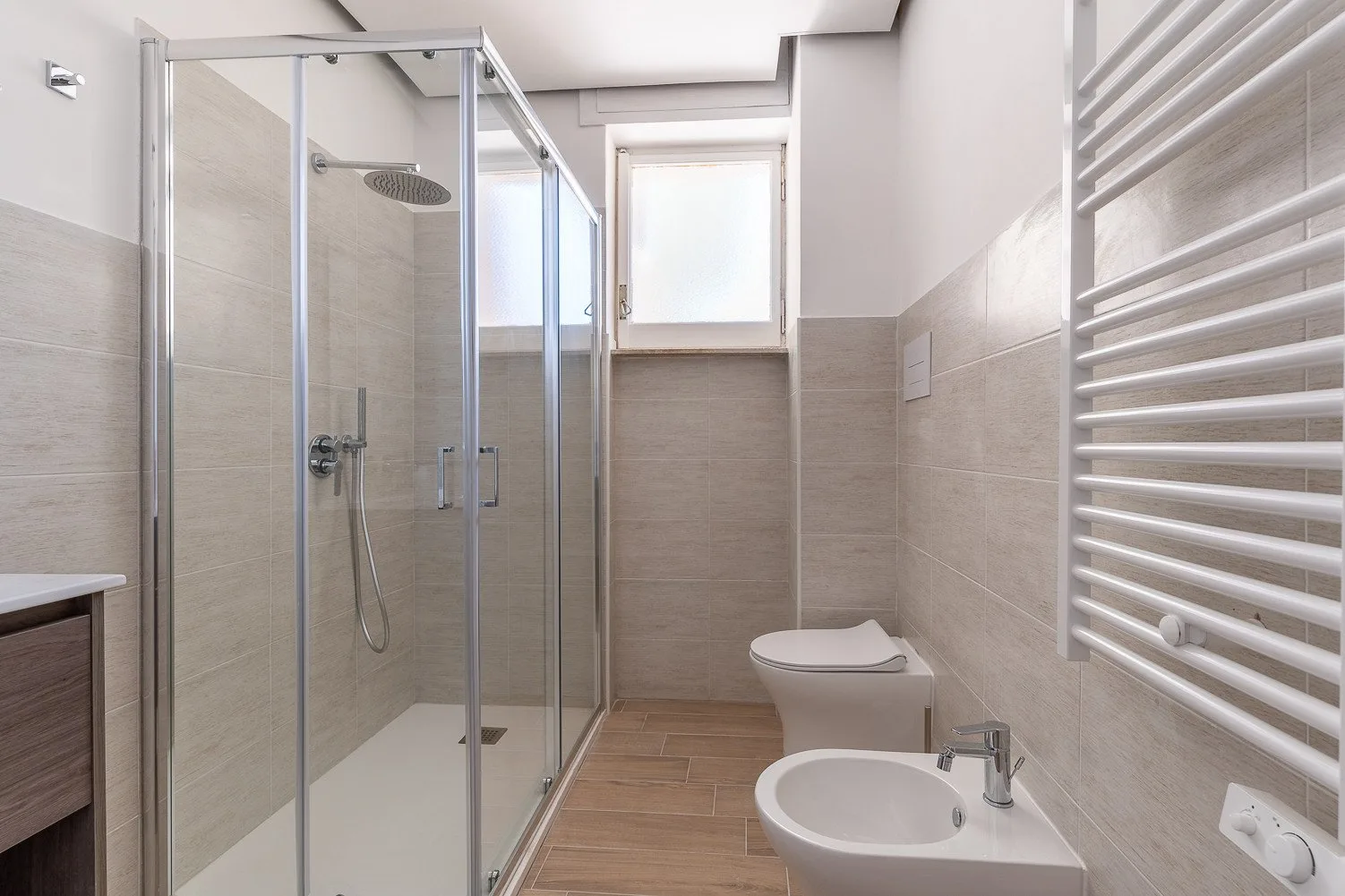 Un baño alicatado con una ducha de vidrio y un inodoro junto a un bidé.