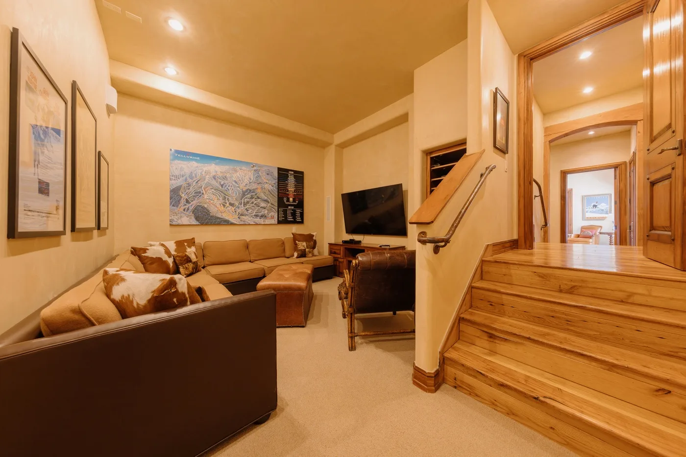 A warm living room with seating, a television, and a wooden staircase.