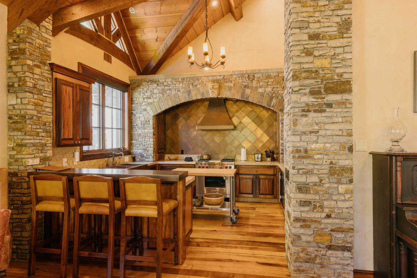 A rustic kitchen with a wooden island, stone walls, and exposed timber beams.