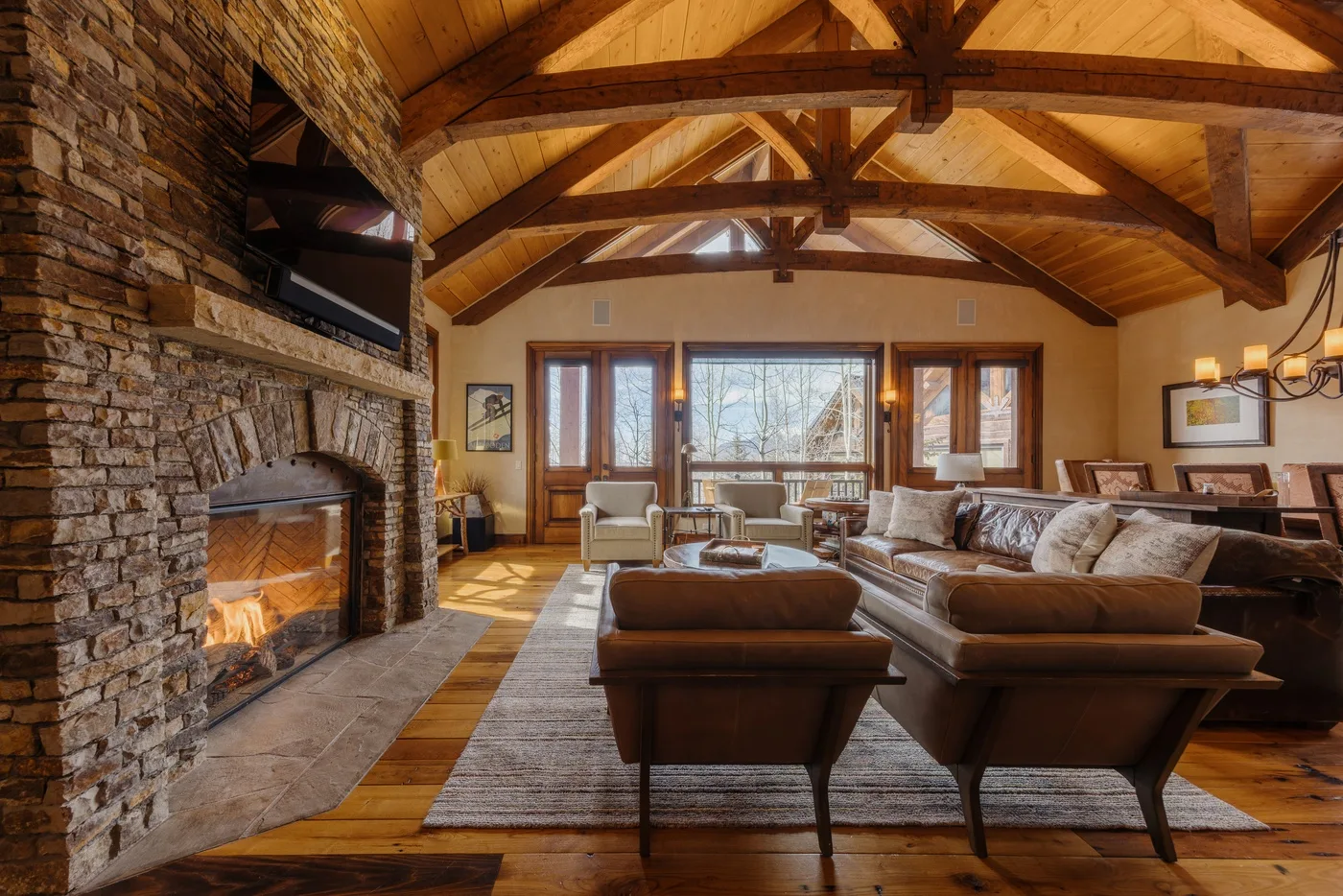 A spacious living room with a stone fireplace and exposed wooden ceiling beams.