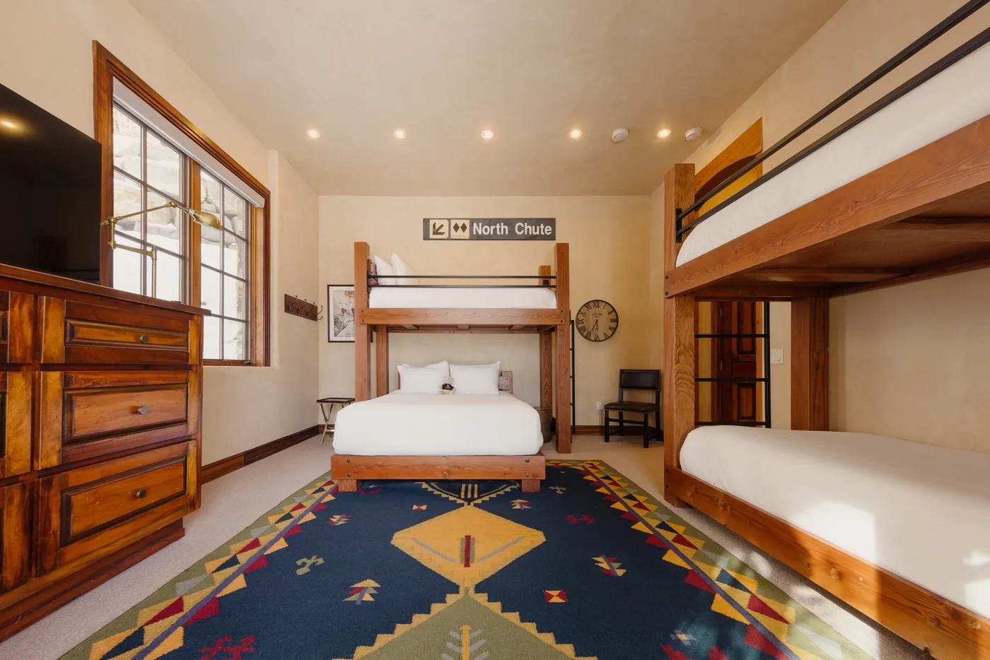 A bedroom with two wooden bunk beds, white bedding, and a colorful patterned rug.