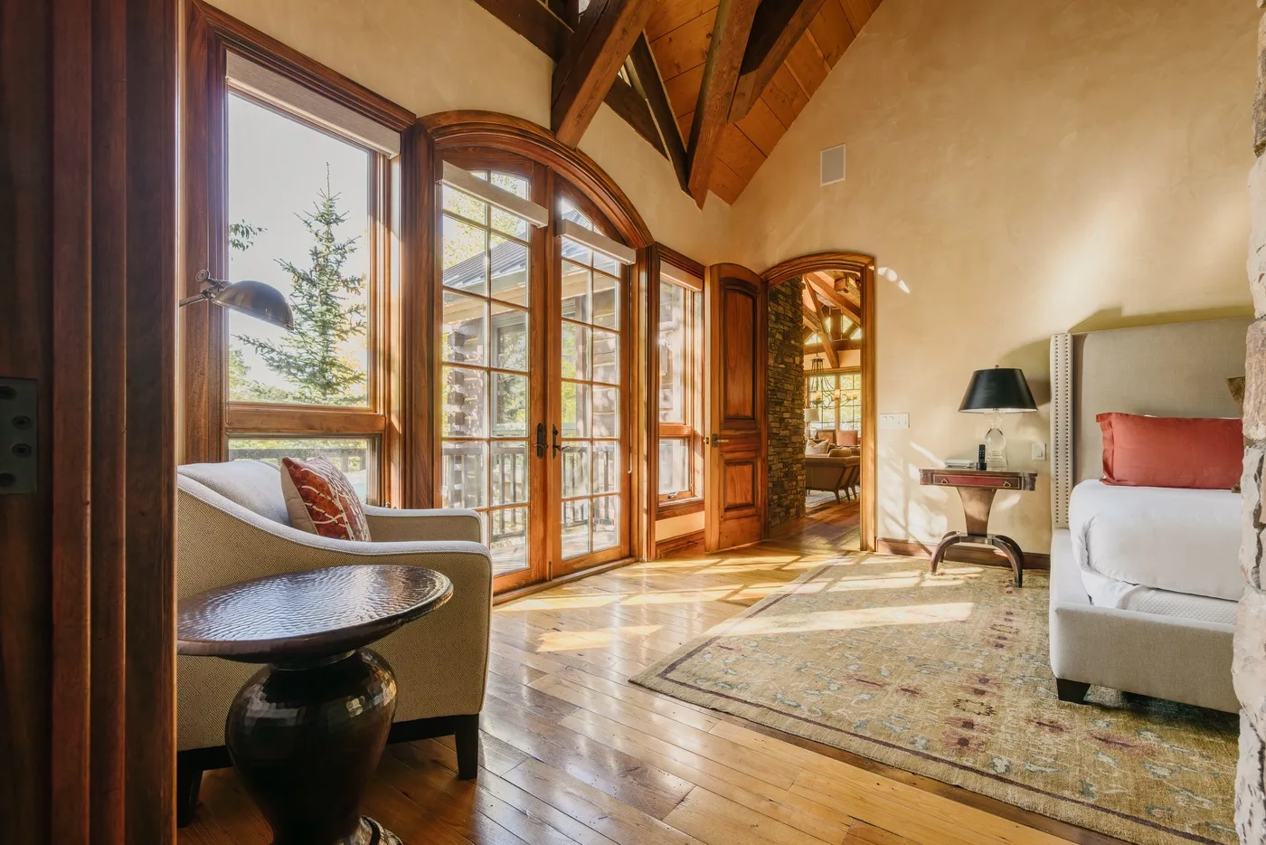 A sunlit living room with tall windows, wood beams, and seating.