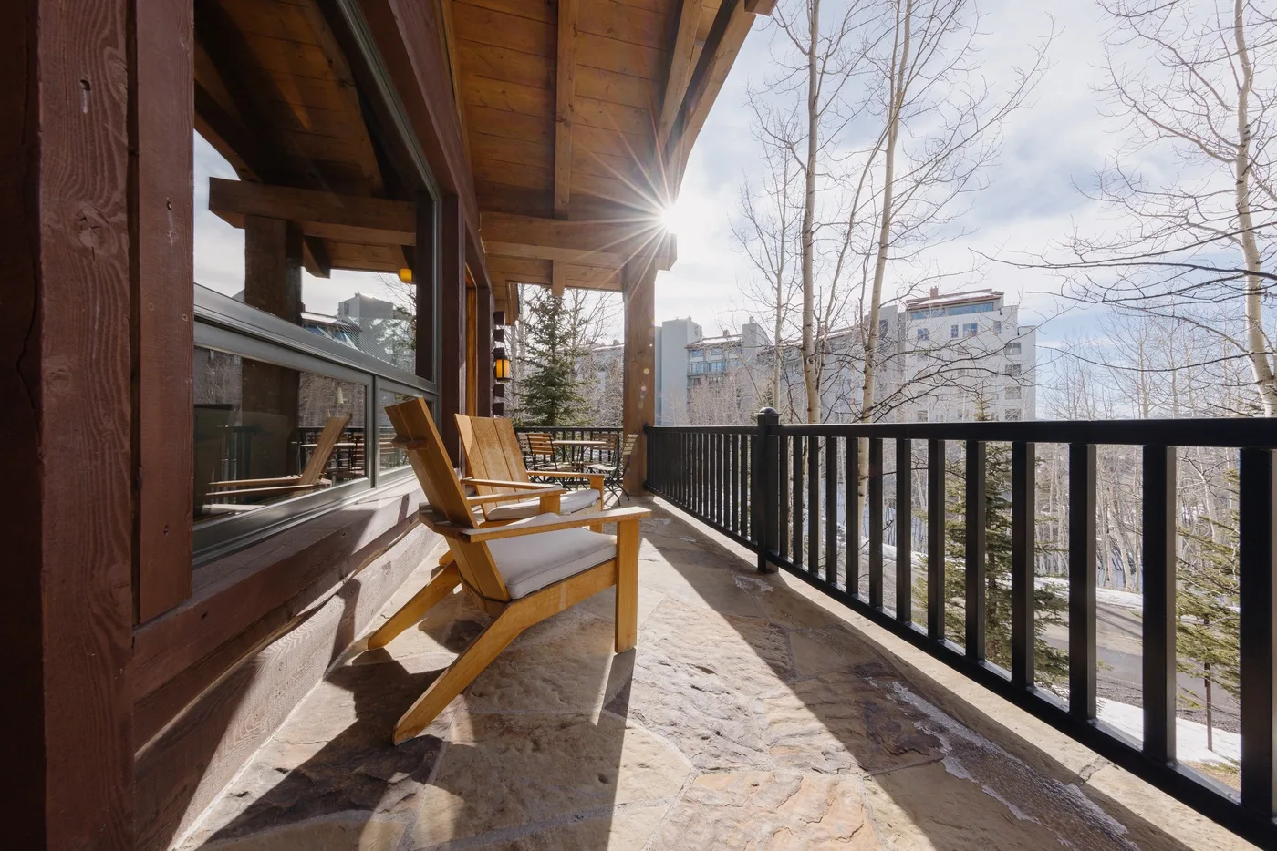 A covered outdoor deck has wooden seating beside a black railing.