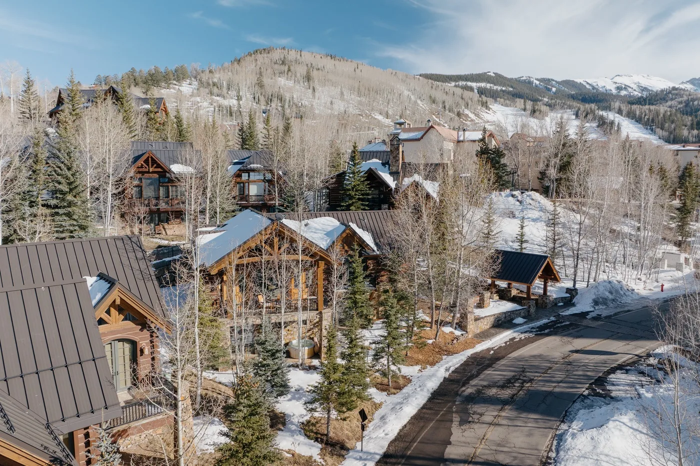 Snow-covered mountain homes sit among trees beside a winding road.