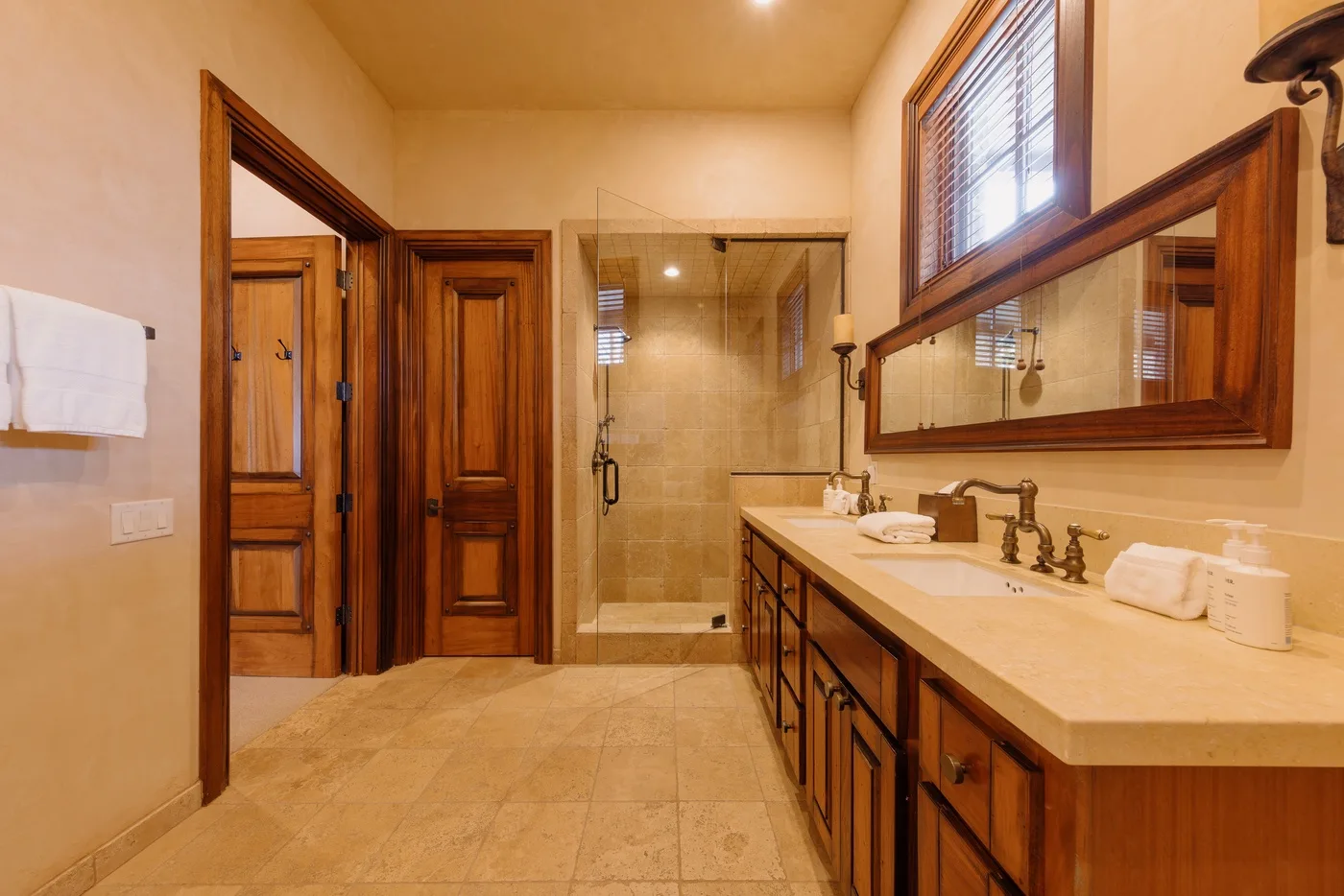A warm-toned bathroom with a glass shower and a long vanity.