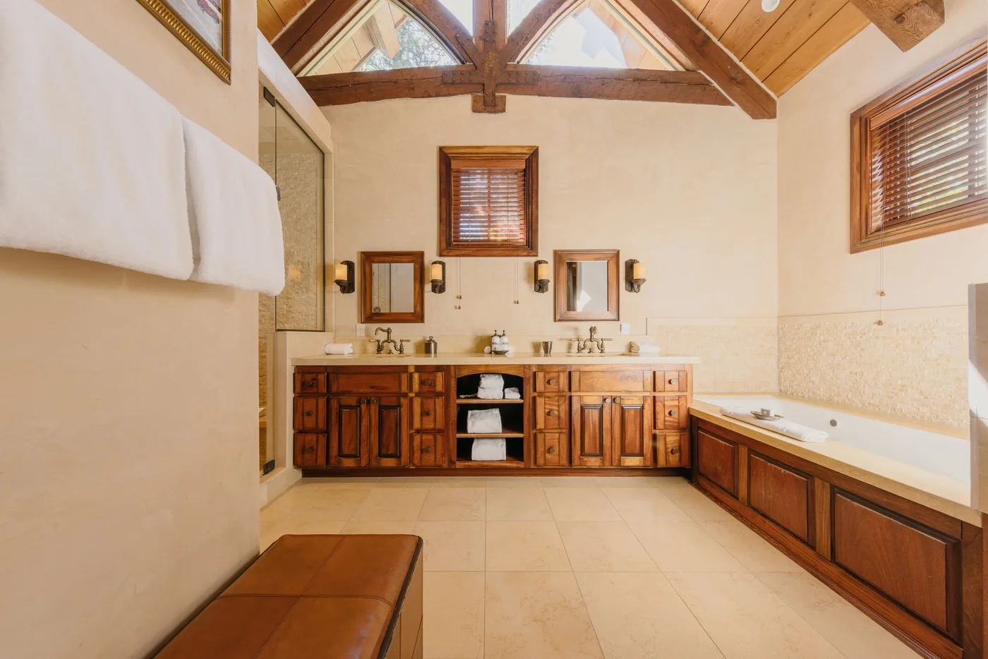 A spacious bathroom with a double vanity, bathtub, and exposed wooden ceiling beams.