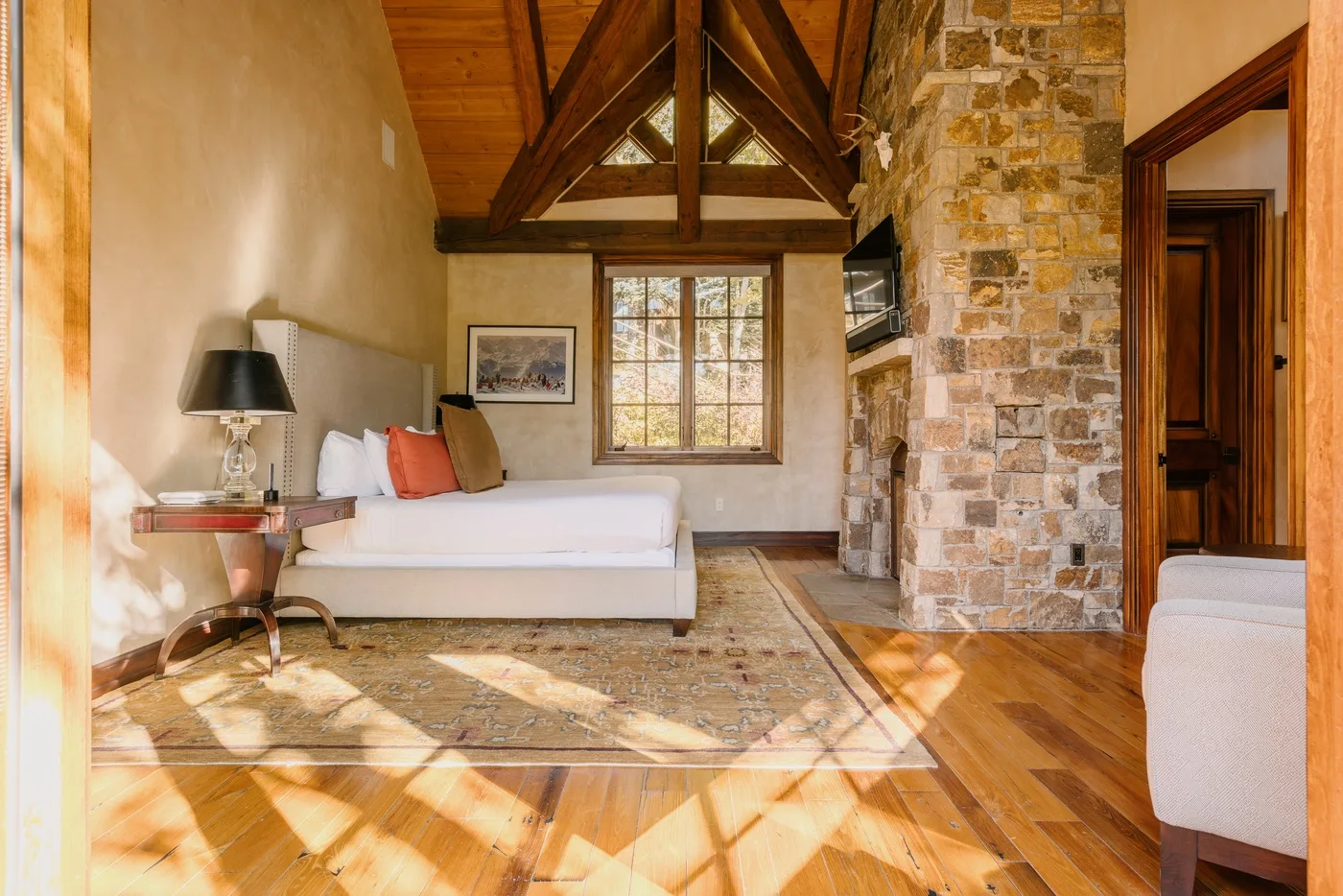 A sunlit living room with seating beneath a high timber-beamed ceiling.