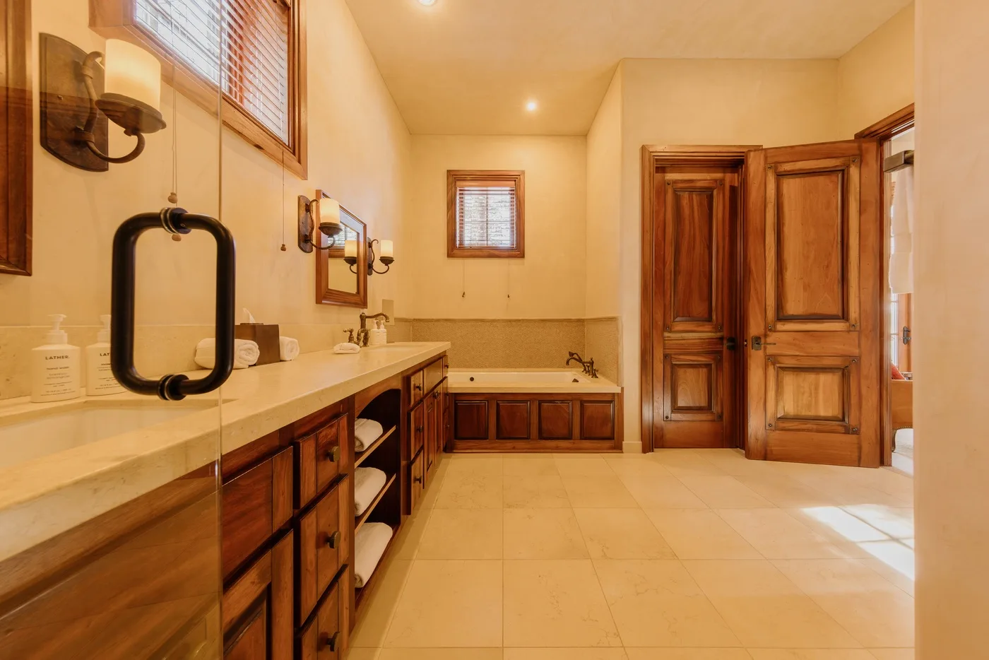 A spacious bathroom with a long vanity, bathtub, and wooden doors.