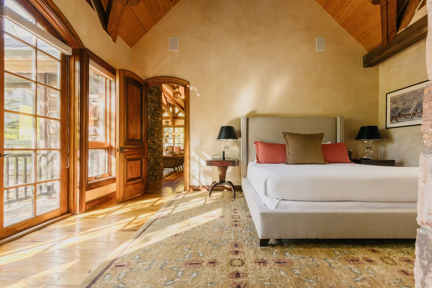 A bedroom with a large bed, wooden ceiling, and tall windows.