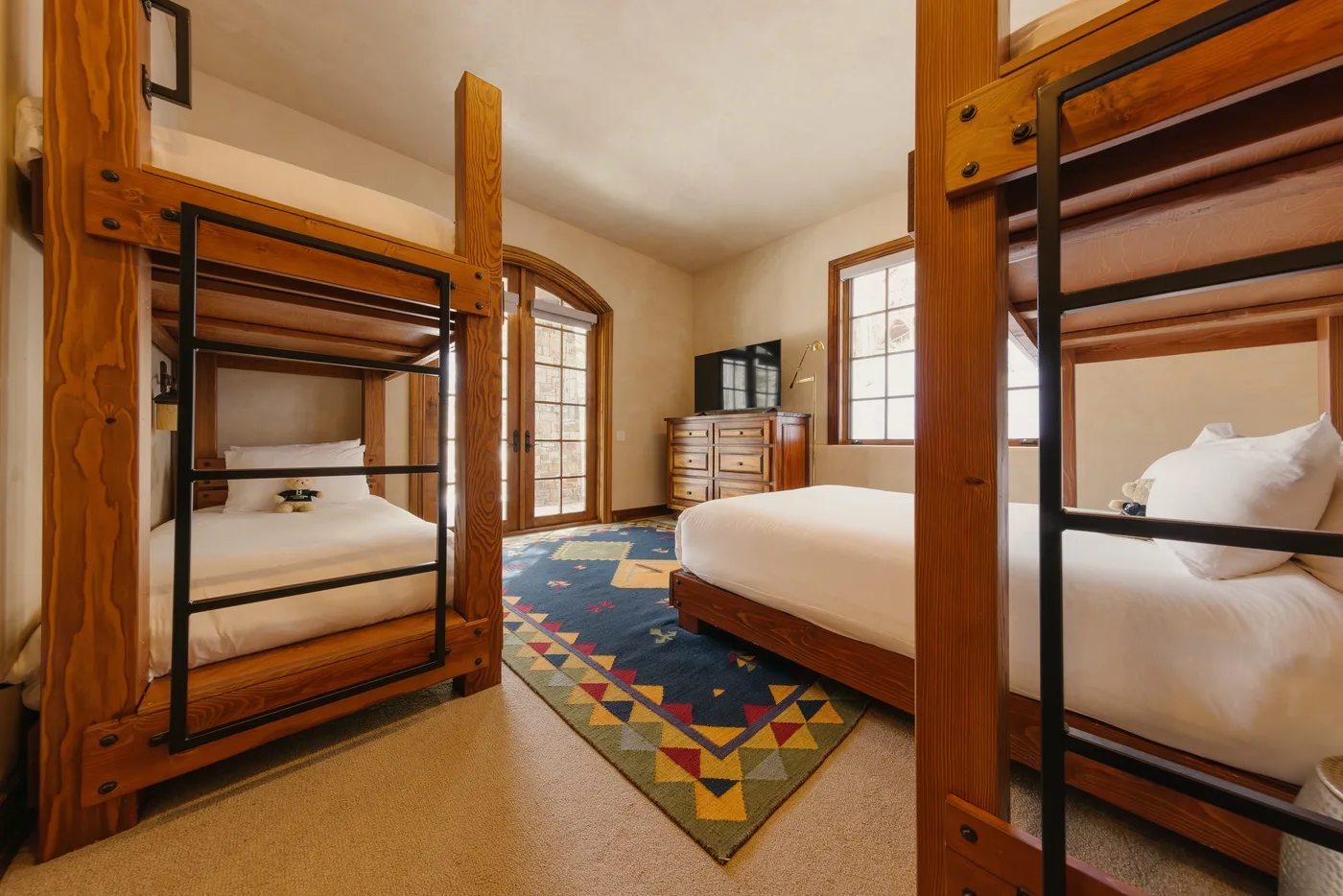 A bedroom with wooden bunk beds, a bed, and a colorful patterned rug.