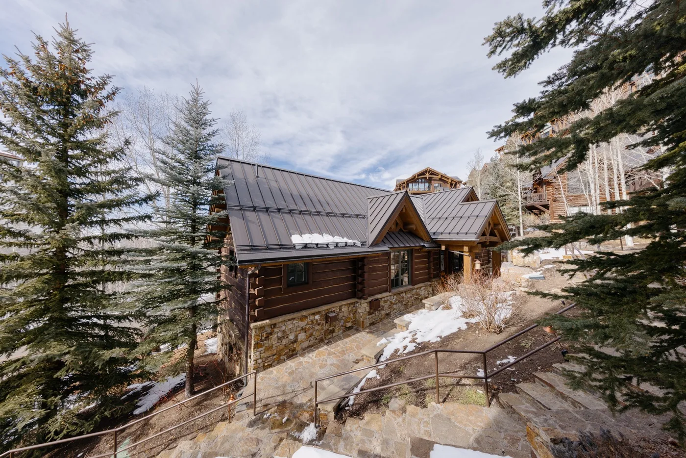 A timber lodge with dark roofs sits among trees on a snowy hillside.