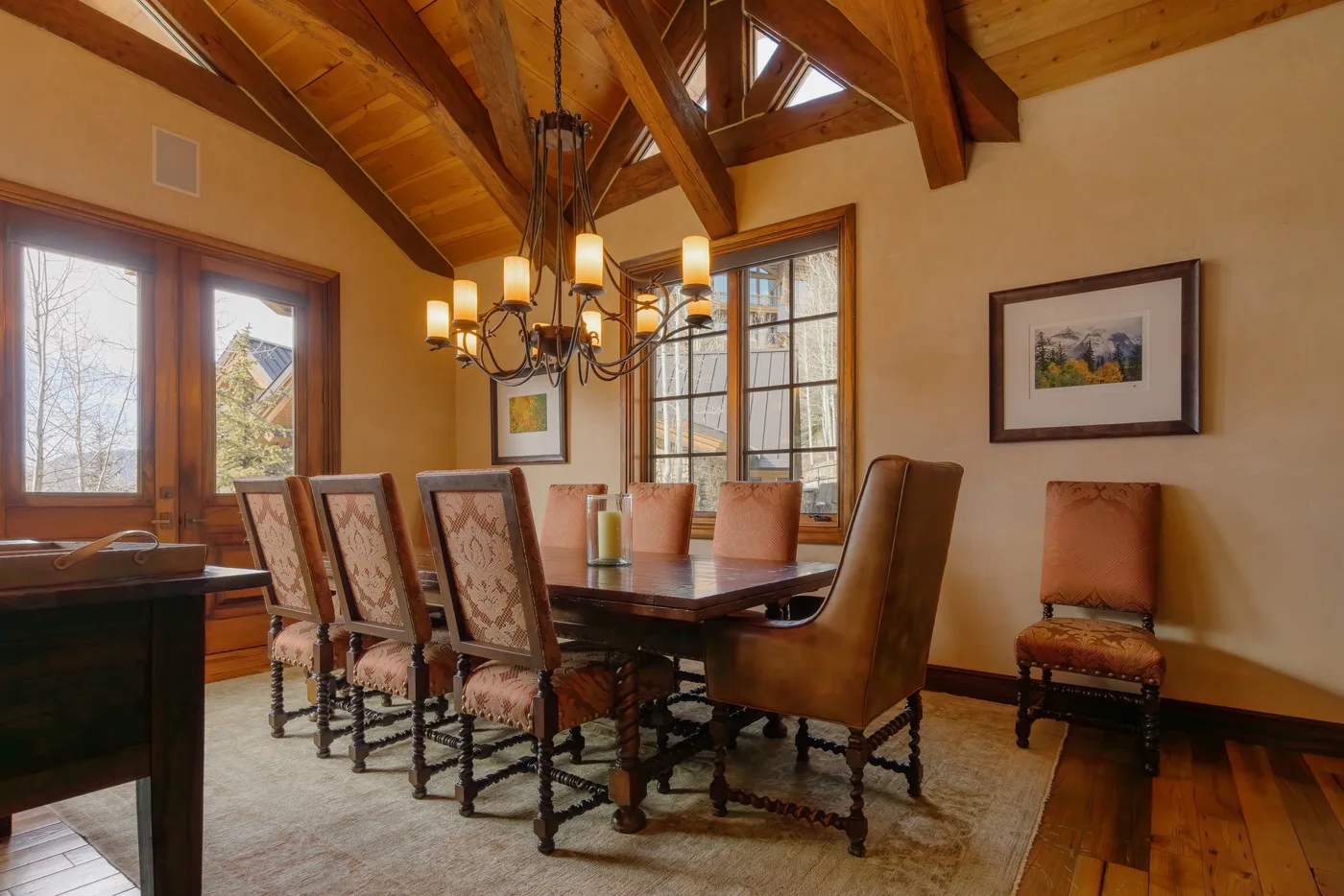A dining room with a wooden table, upholstered seating, and a chandelier.