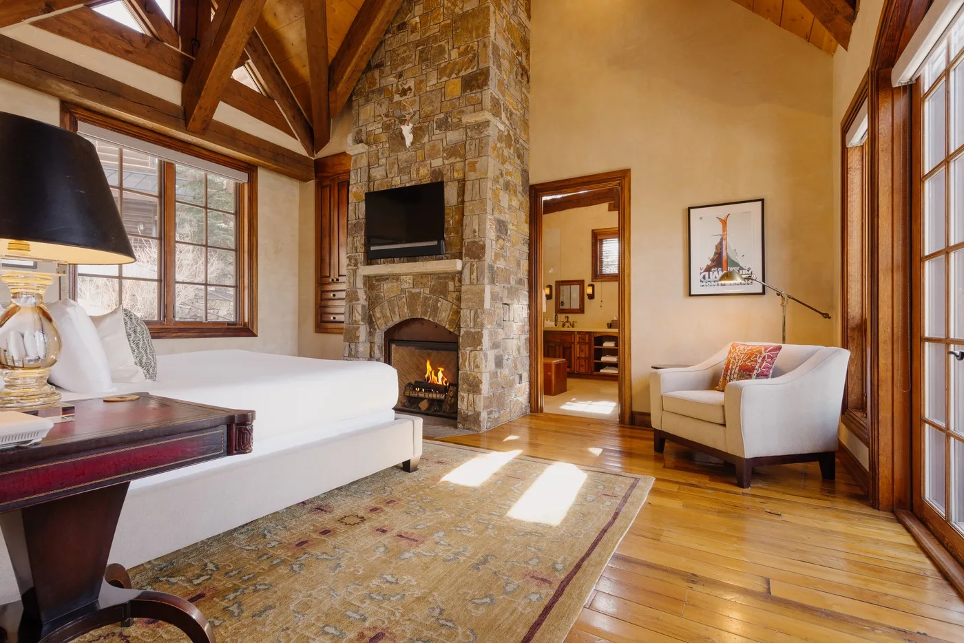 A living room with a stone fireplace, seating, and exposed wooden ceiling beams.
