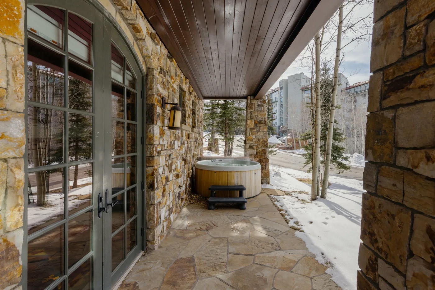 A covered stone patio with a hot tub beside glass doors.