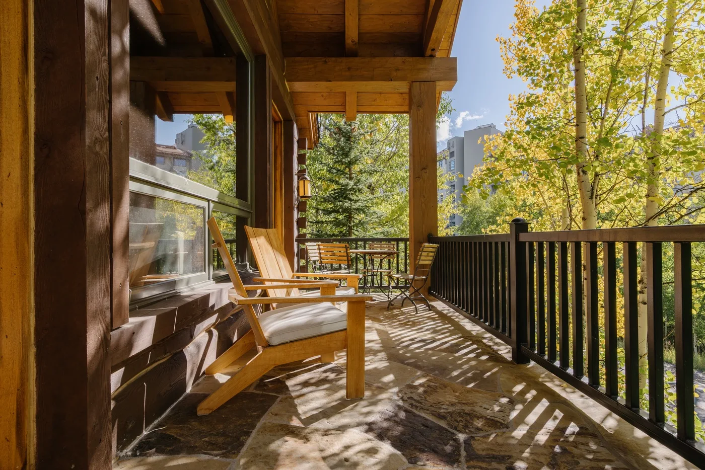 A covered wooden deck with outdoor seating overlooks leafy trees.