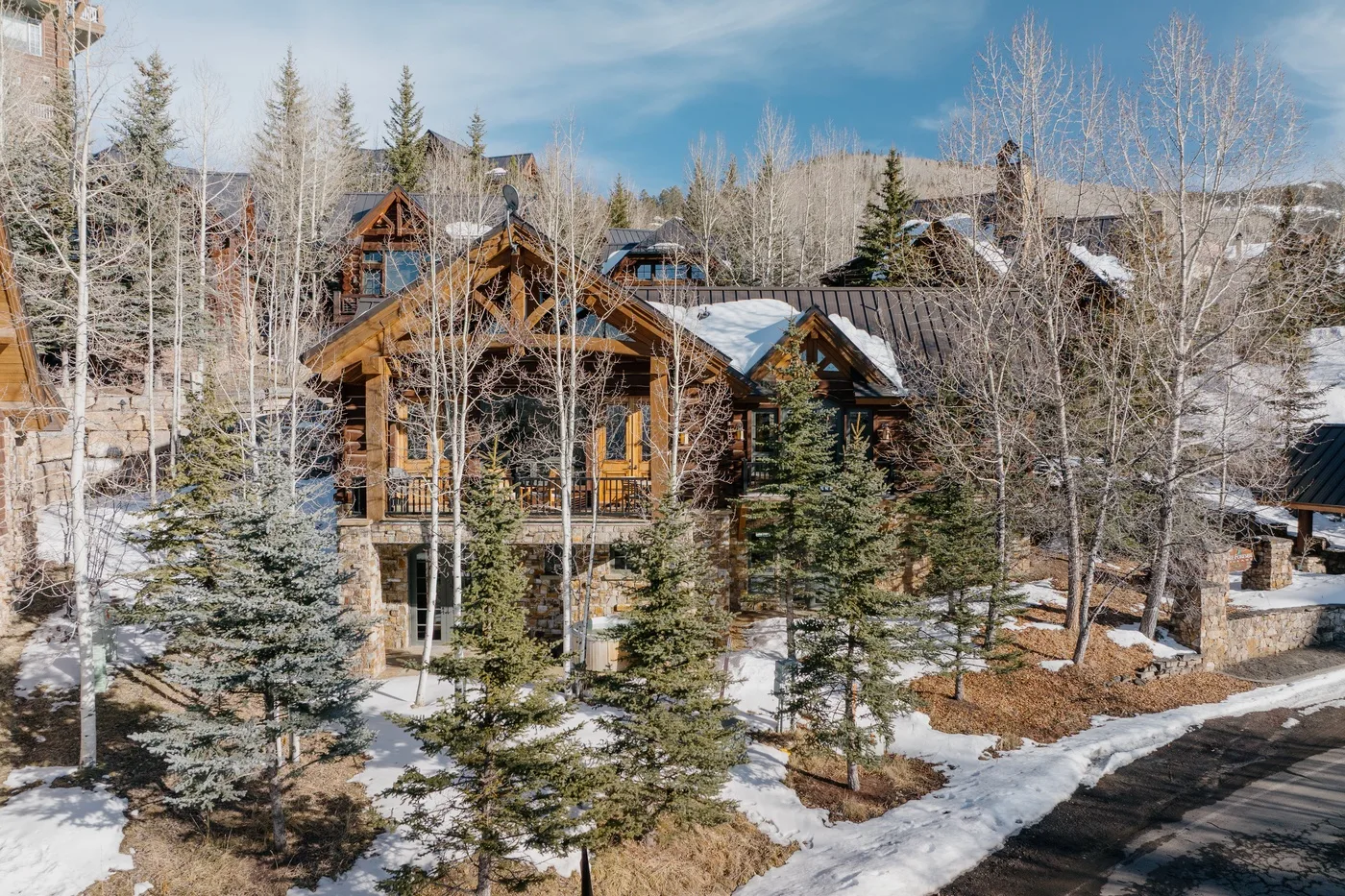 A timber lodge sits among leafless trees and evergreens beside a snow-lined road.