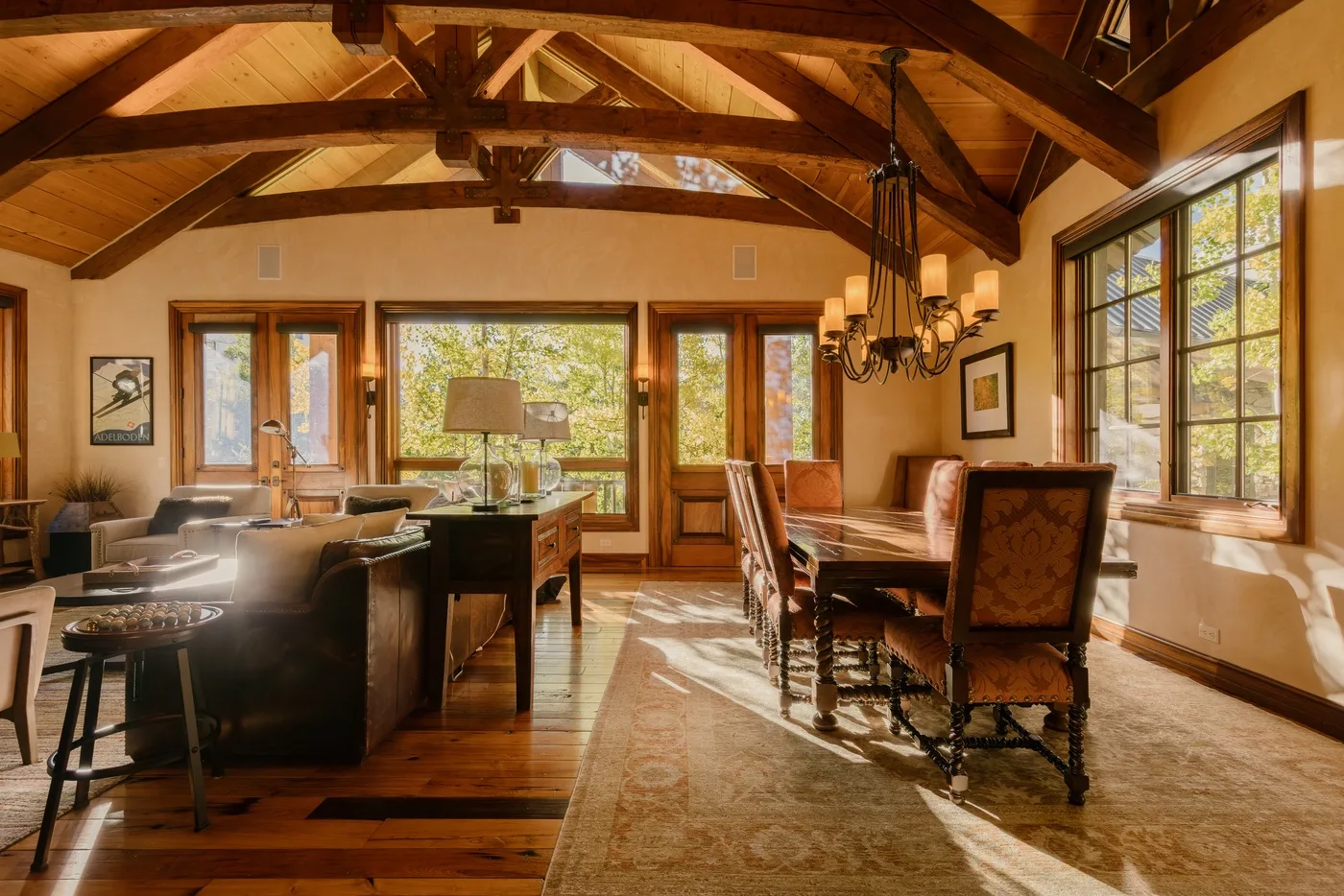 A bright open-plan living and dining room with exposed wooden ceiling beams and large windows.
