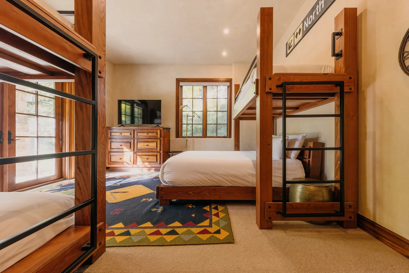 A bedroom with wooden bunk beds, a dresser, and a colorful rug.