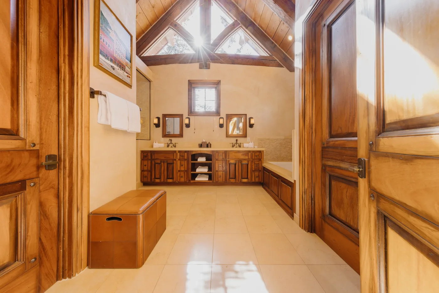A wood-paneled bathroom has a double vanity, tiled floor, and high peaked ceiling.