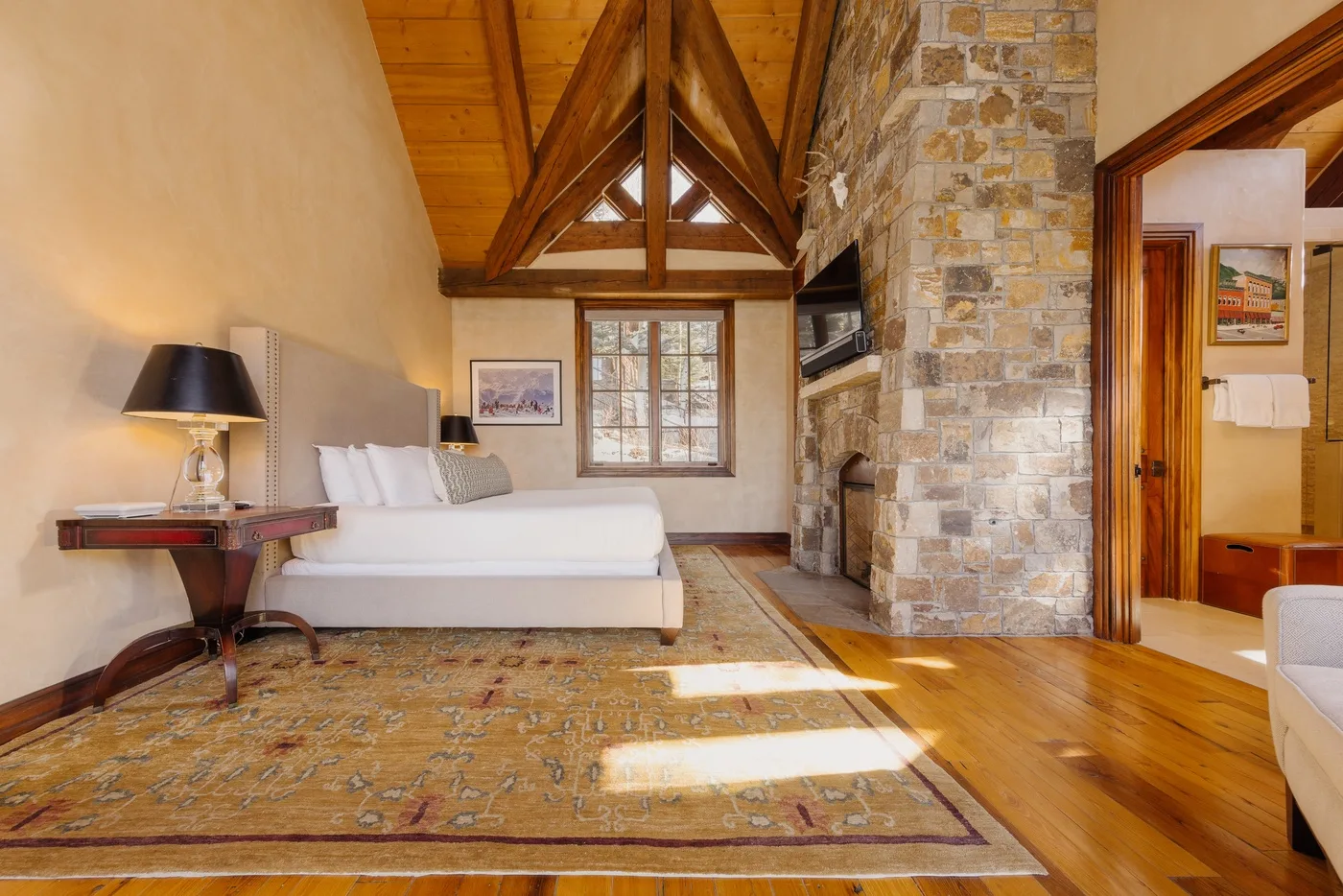 A bedroom with a bed, a stone fireplace, and exposed wooden ceiling beams.