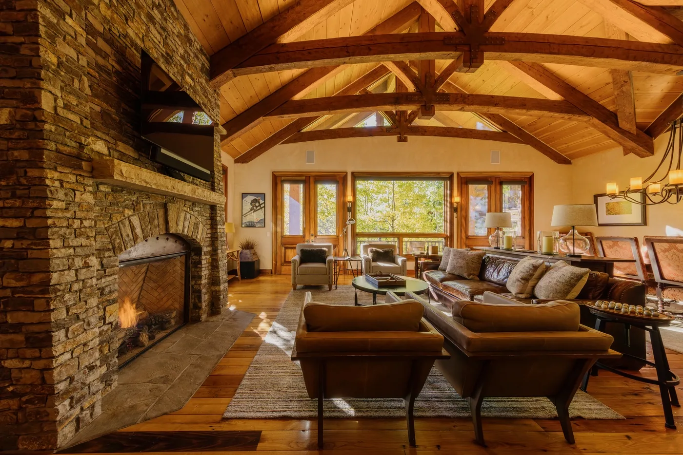 A spacious living room with a stone fireplace, wood beams, and seating around a coffee table.