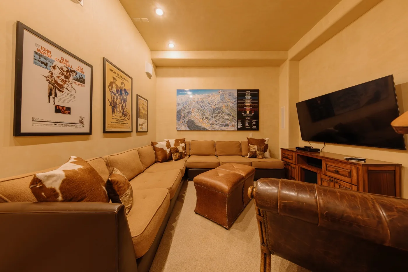 A warm-toned living room with sectional seating, framed artwork, and a television.