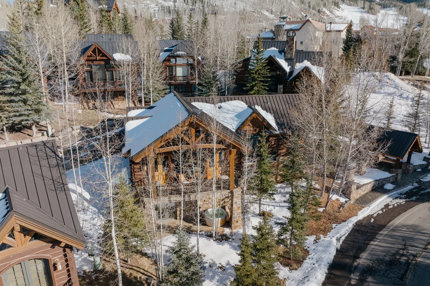 Snow-covered wooden buildings sit among trees beside a curved road.