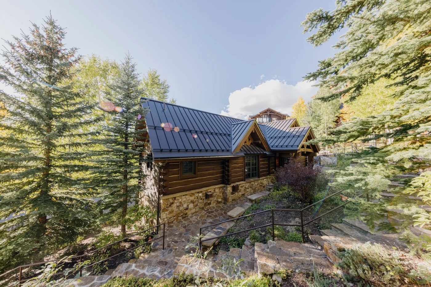 A rustic cabin sits among tall trees beside a stone walkway.