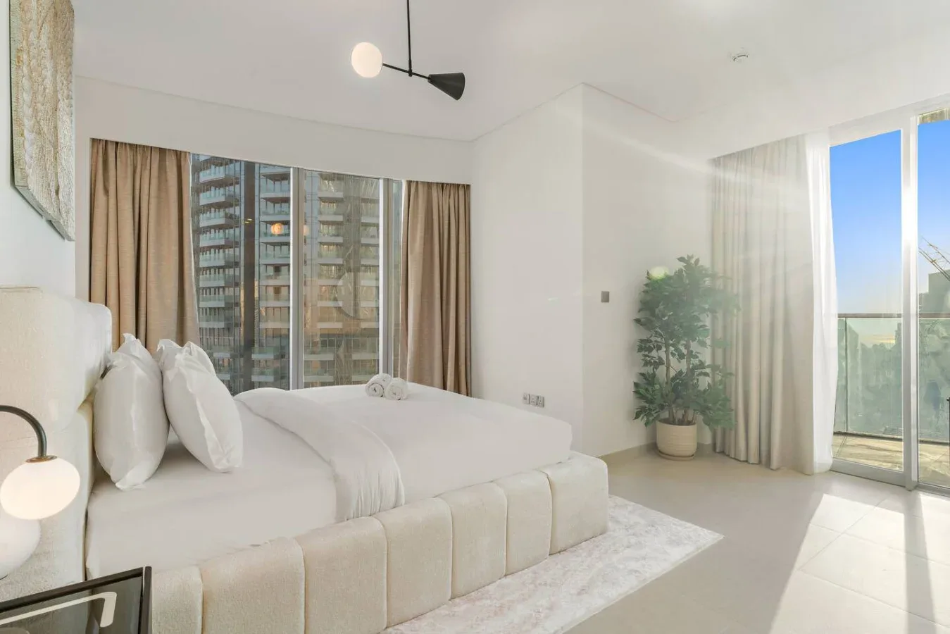A bright bedroom with a large bed beside floor-to-ceiling windows.
