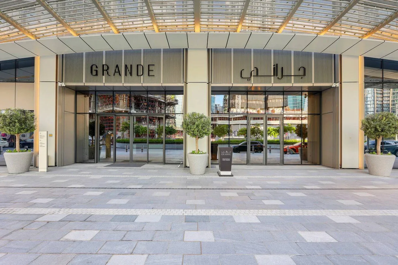 A glass-fronted building entrance sits beneath a broad canopy, with planters beside the doors.