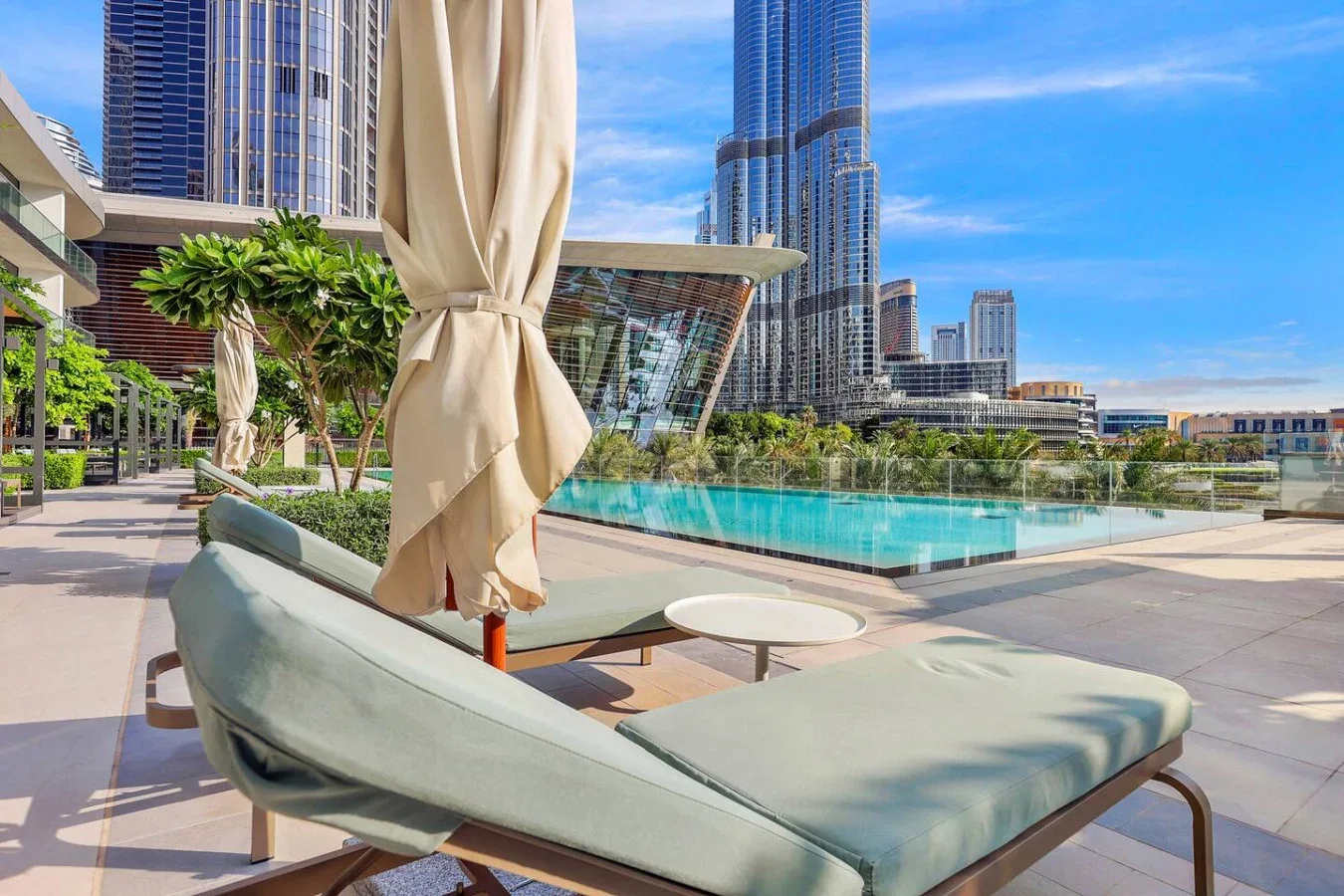 An outdoor pool terrace with lounge seating and tall city buildings in the background.
