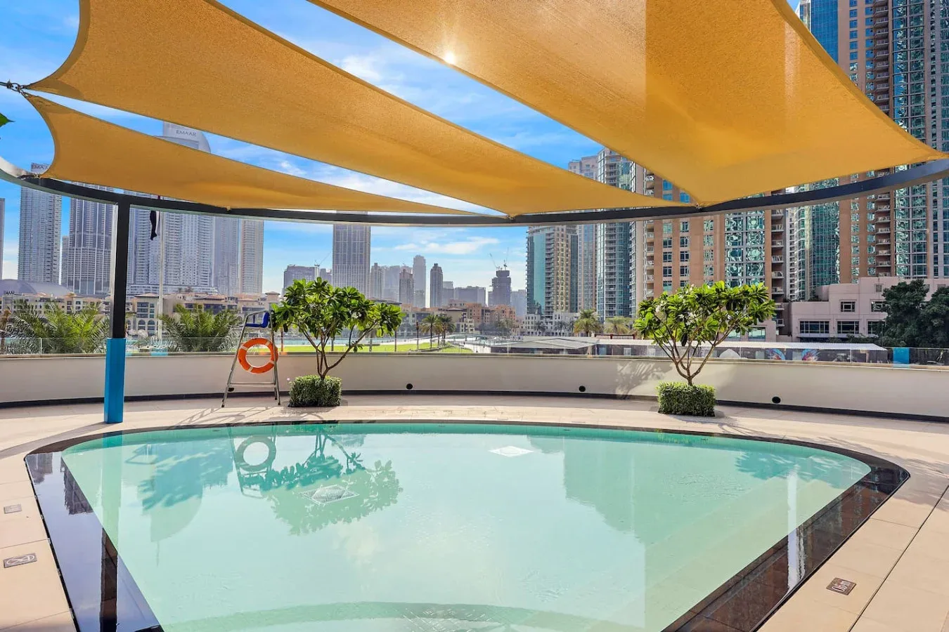 A rooftop pool sits beneath shade sails, with high-rise buildings visible beyond.