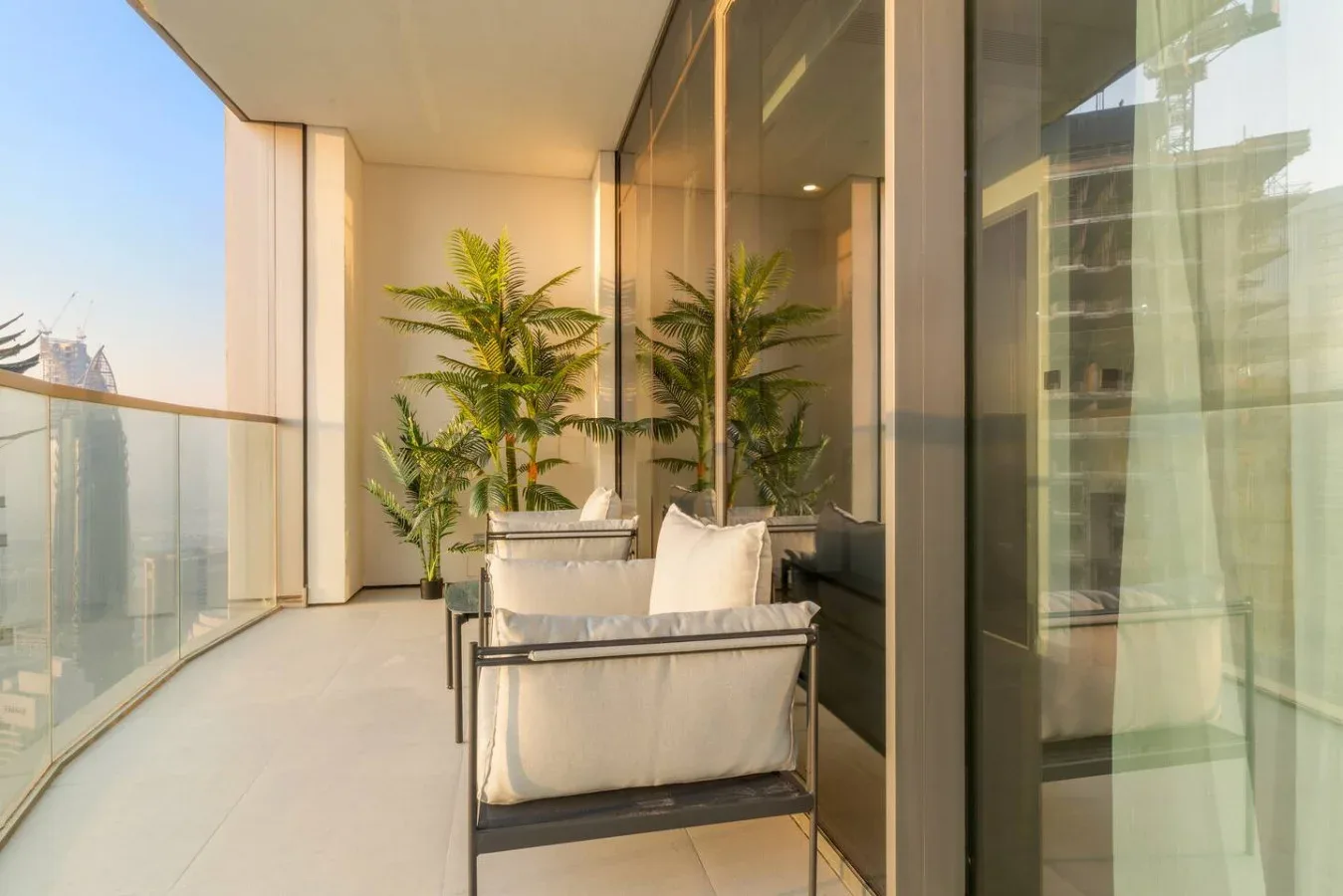 A glass-sided balcony with cushioned seating and potted plants.