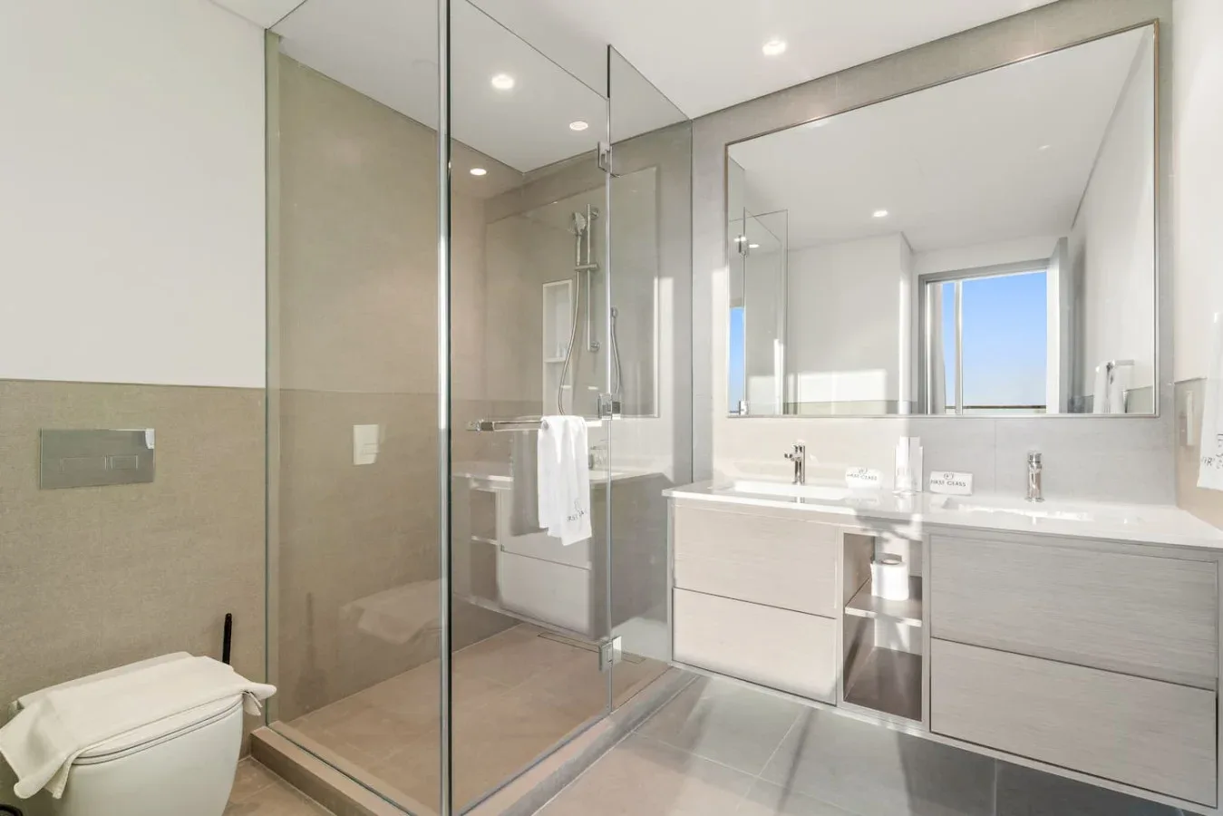 A bright bathroom with a glass shower and a double-sink vanity.
