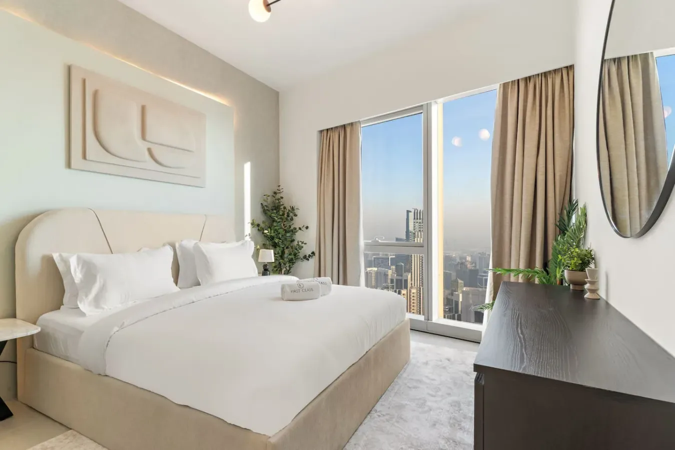 A bright bedroom with a neatly made bed beside floor-to-ceiling windows.