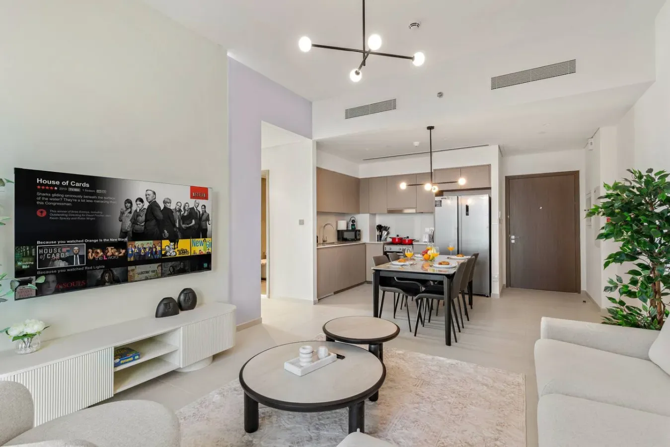 A bright open-plan living area with a dining table and kitchen in the background.
