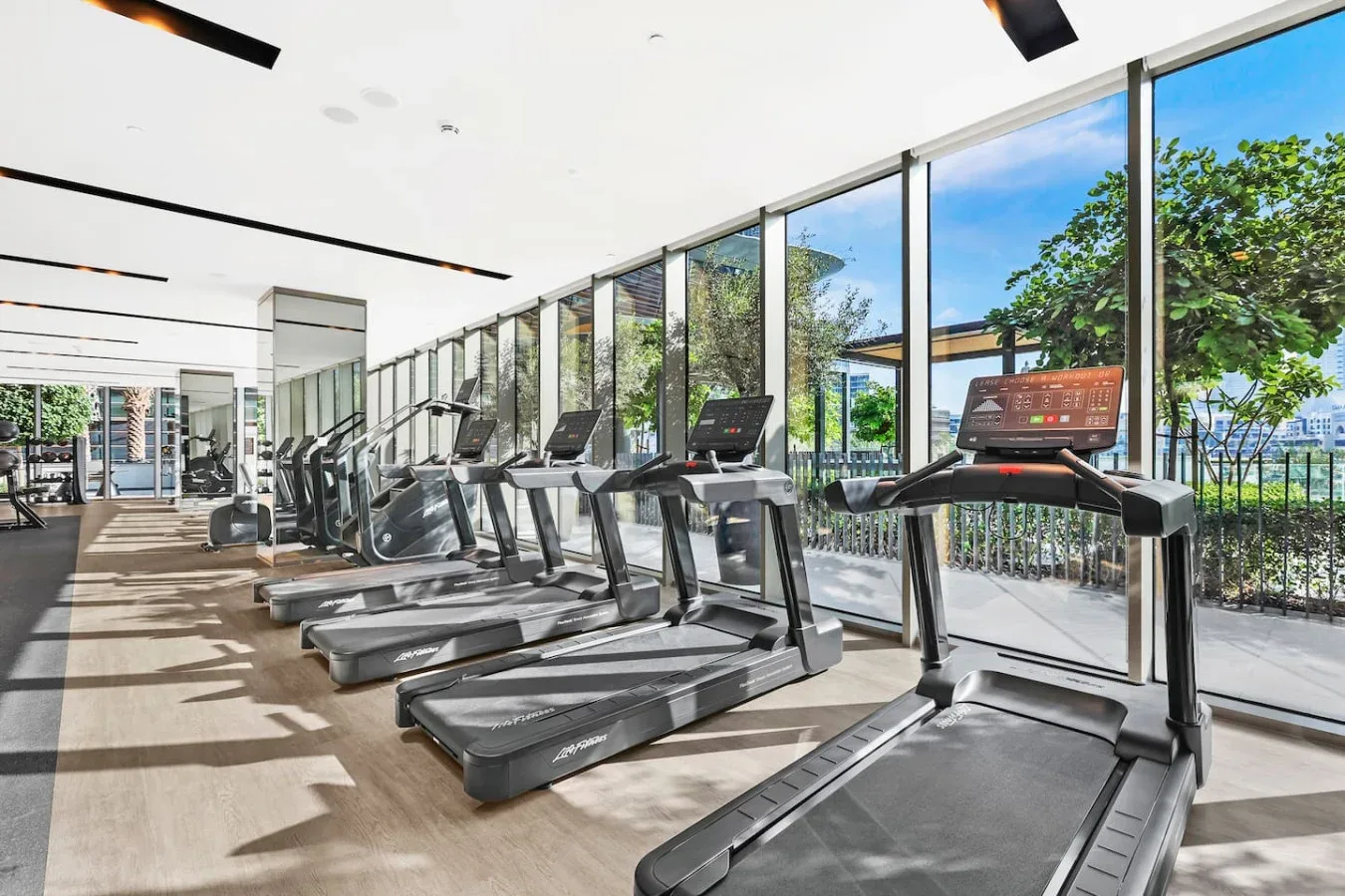 A gym with treadmills arranged beside large windows overlooking greenery.