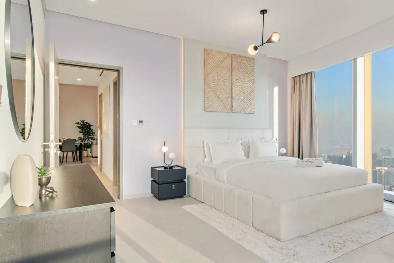 A bright bedroom with a large bed beside floor-to-ceiling windows.