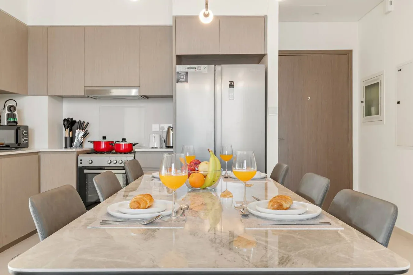 A dining table set for a meal sits in a bright kitchen with cabinets and appliances.