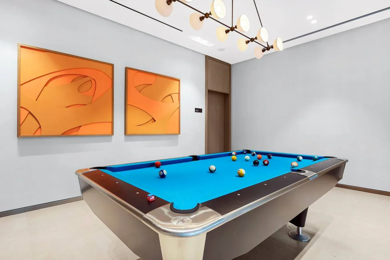 A billiards room with a blue-felt pool table and orange abstract artwork.